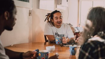 People sat round a table chatting with hot beverages